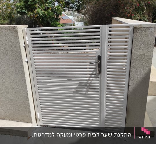 שער מתכת אפור עם ידית על קיר בטון